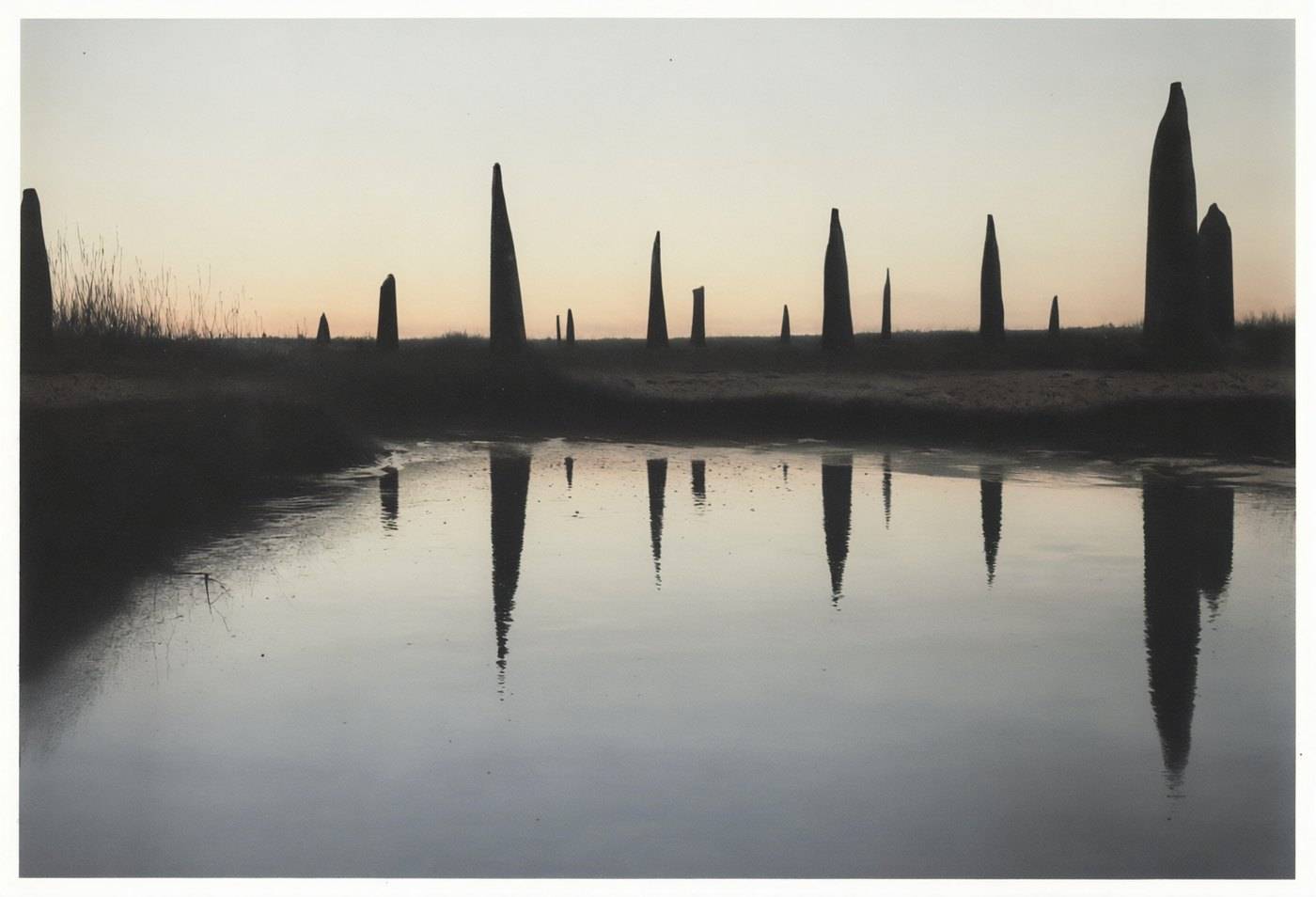 Pale mist over flat water with a row of tall dark posts standing in it, mirrored in the surface.